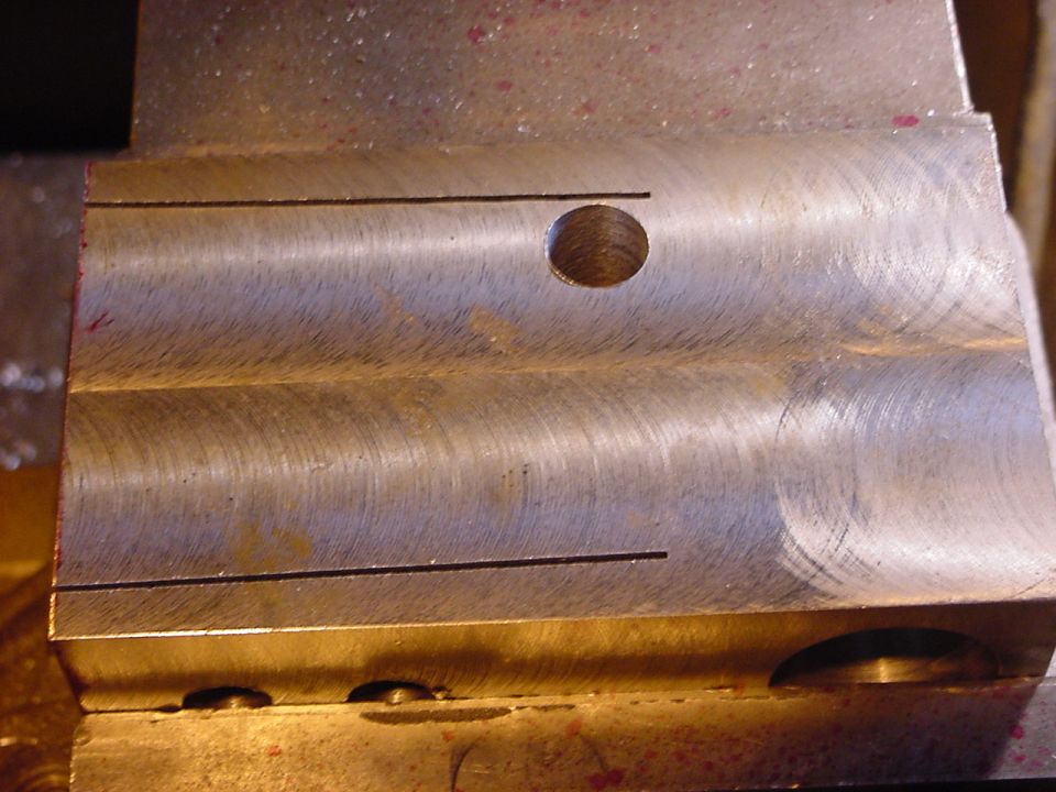 Machined metal part with a hole and two parallel lines, Supermotors.net logo visible