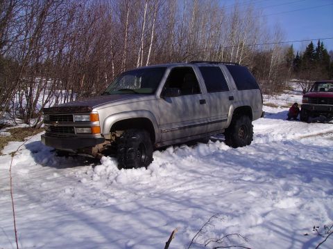 2000 Chevrolet Tahoe - A lifted SUV is stuck in deep snow off-road, with a red truck visible in the background.