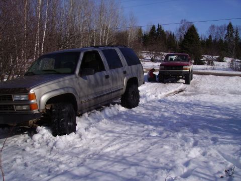 2000 Chevrolet Tahoe - A silver SUV is stuck in the snow next to a red pickup truck.