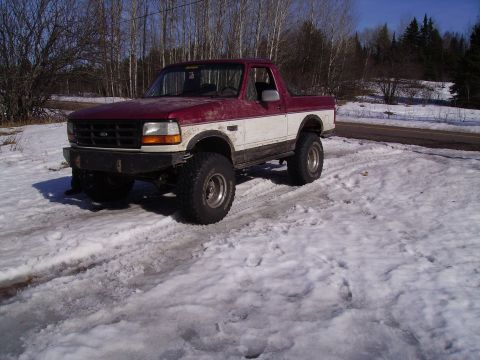 2000 Chevrolet Tahoe - A modified Ford Bronco sits in a snowy, wooded area with a road in the background.