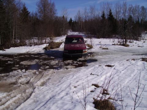 2000 Chevrolet Tahoe - A red van navigates a partially frozen road surrounded by snow and trees.