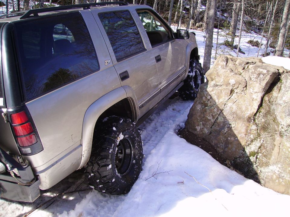 2000 Chevrolet Tahoe navigating a snowy trail with large tires, close to a rock