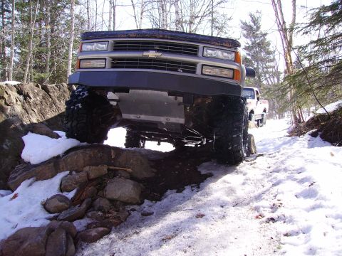 2000 Chevrolet Tahoe - A modified Chevrolet pickup truck navigates a snowy, rocky trail with another truck visible in the background.