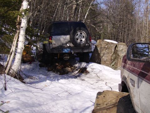 2000 Chevrolet Tahoe - Two vehicles navigate a snowy, wooded terrain with large rocks.