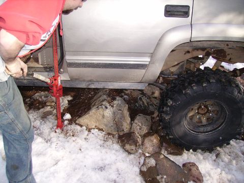 2000 Chevrolet Tahoe - A person uses a Hi-Lift jack to free a silver SUV stuck on rocks in a snowy environment.