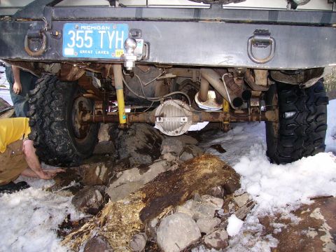 2000 Chevrolet Tahoe - The rear axle and suspension of a truck are visible, with large tires stuck in snow and rocks.