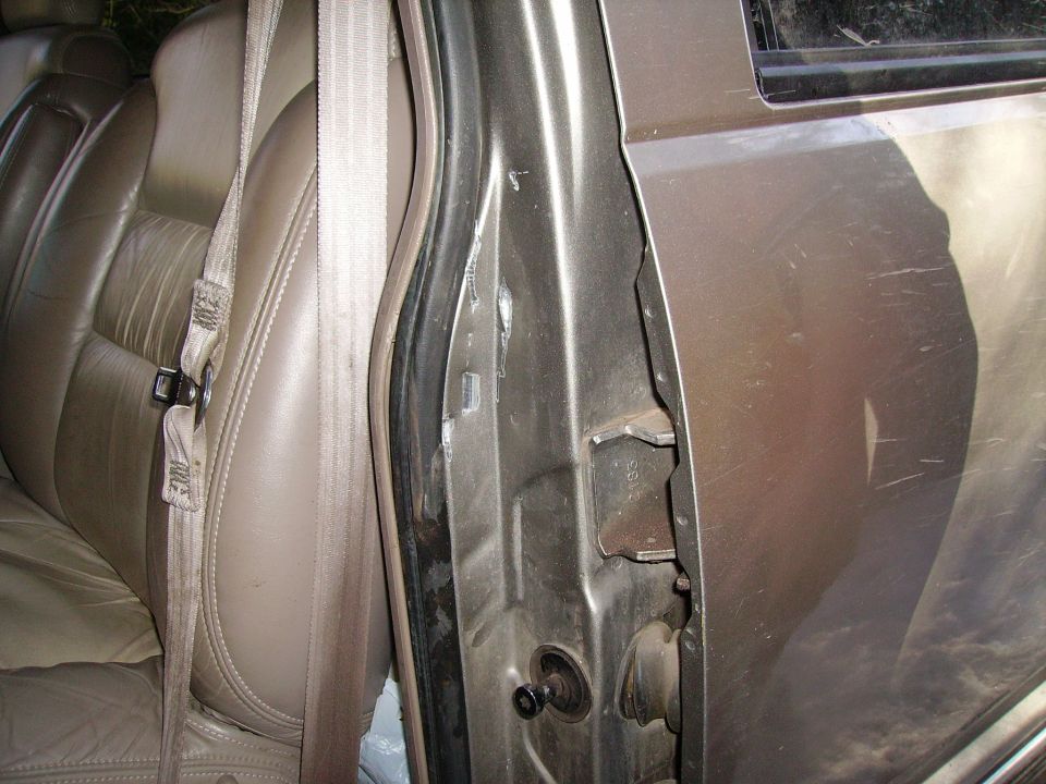 Brown leather interior with beige seatbelt, open driver's side door showing damage to the frame