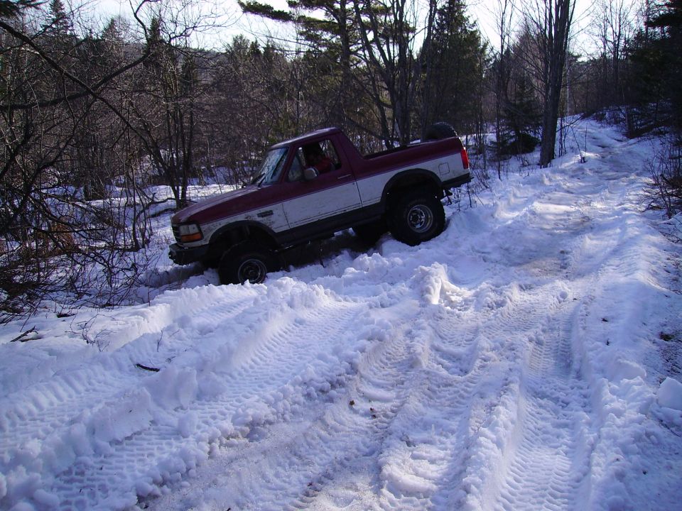 Maroon and white pickup truck with off-road tires driving on a snowy trail