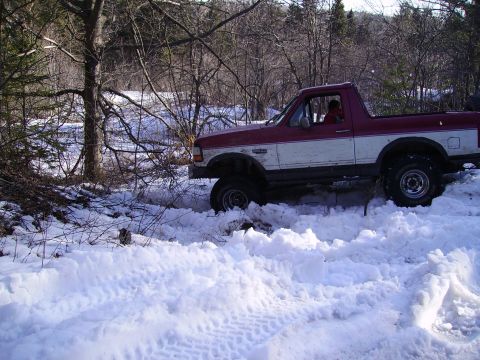 2000 Chevrolet Tahoe - A two-tone pickup truck is stuck in deep snow off-road, surrounded by trees and brush.