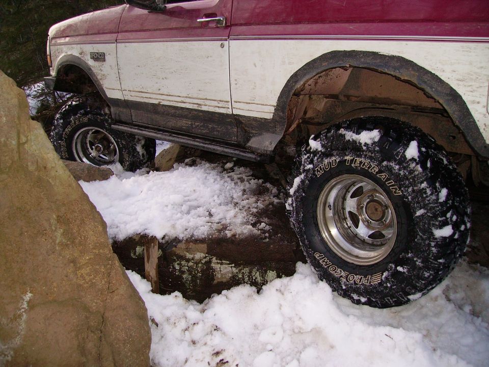 Red and white Ford Bronco with off-road tires navigating snow and rocks