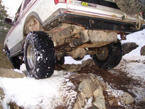 2000 Chevrolet Tahoe - A white and maroon pickup truck navigates a rocky, snowy trail, showing its rear axle and suspension system.