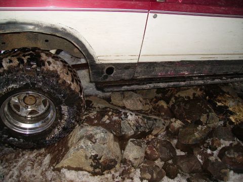 2000 Chevrolet Tahoe - Close-up of a vehicle's side, showing a tire and fender, on a rocky, snowy terrain.