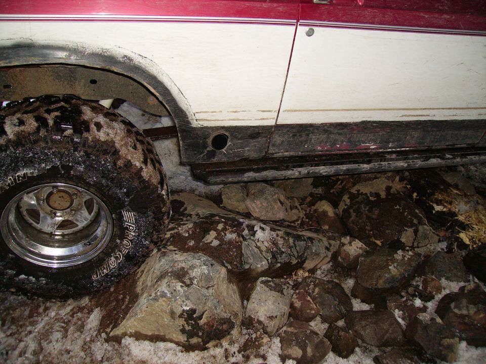 Off-road tire with "PRO COMP" visible, next to a white and red vehicle body over rocks and snow