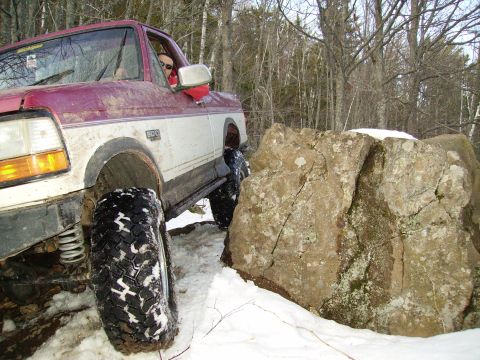2000 Chevrolet Tahoe - A red and white pickup truck with off-road tires maneuvers through a snowy, rocky landscape.