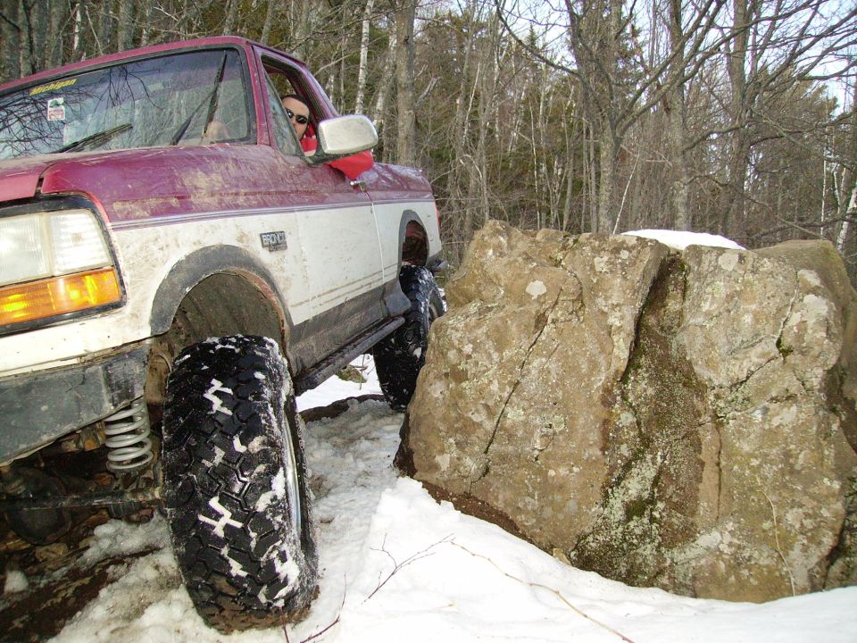 Red and white pickup truck navigating rocky terrain in snow. Visible badge reads '4.9L'
