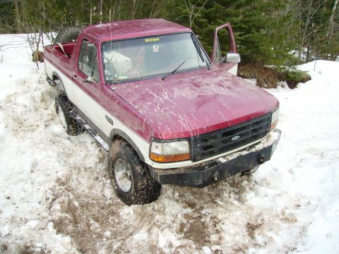 2000 Chevrolet Tahoe - This two-tone Ford Bronco is stuck in a snowy, wooded area with its driver's door open.