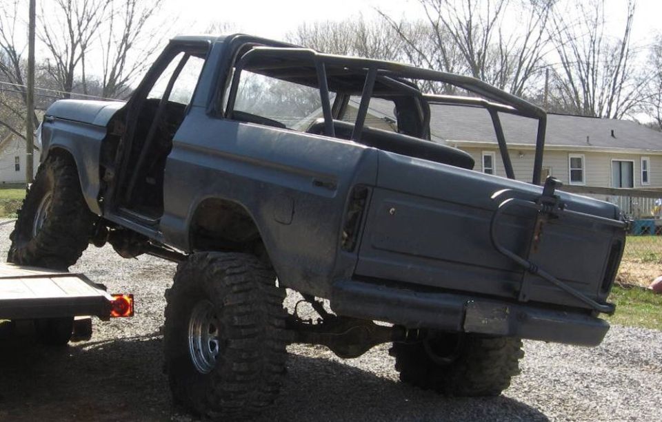 Dark gray 1979 Ford Bronco with roll cage and off-road tires on a trailer