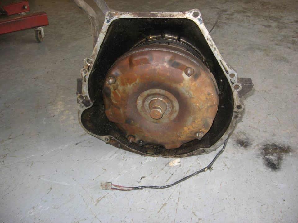 Automatic transmission with rusty torque converter in bellhousing sitting on concrete shop floor