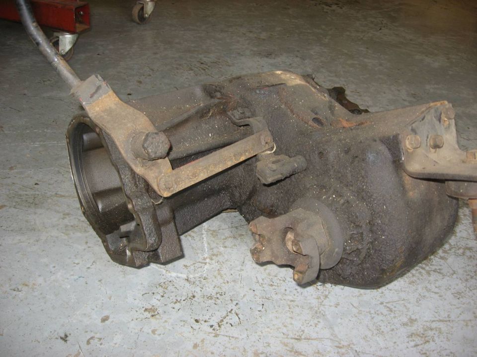 Removed cast-iron manual transmission with shift linkage lying on concrete shop floor