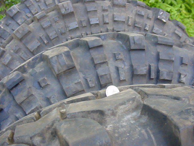 Close-up of aggressive mud-terrain tire tread with a coin placed on it for scale