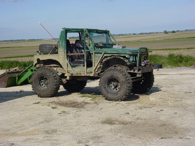 Green off-road vehicle with large tires and a front loader, seen from the front-right