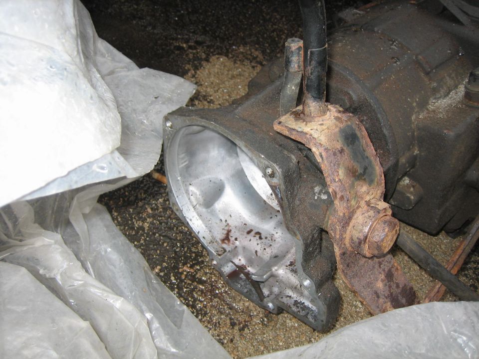 Close-up of a rusty metal bracket attached to a transfer case part, with white plastic sheeting nearby