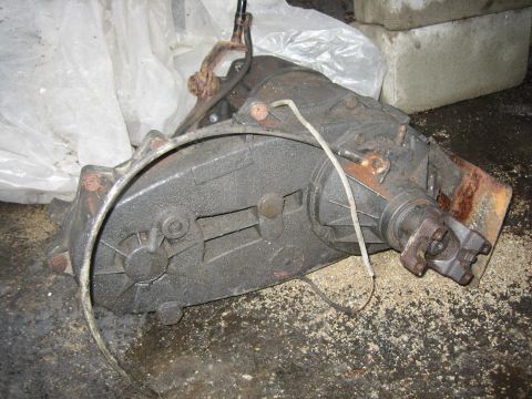 1994 Ford Bronco - A used transfer case, covered in grease and showing signs of rust, sits on a floor with debris.