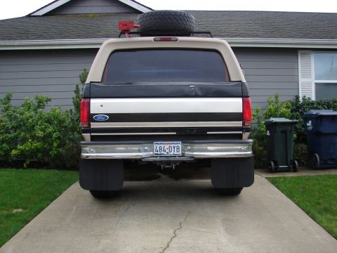 1996 Ford Bronco - Rear view of a 1996 Ford Bronco parked in a driveway, showing its spare tire on the roof rack.