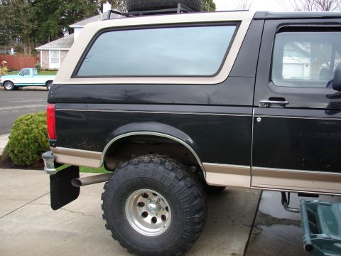 1996 Ford Bronco - A lifted black and tan Ford Bronco is parked on a driveway, with a light blue pickup truck in the background.