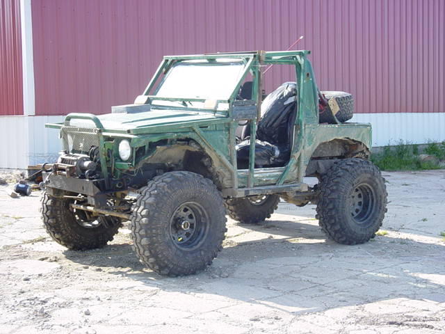 Green modified off-road vehicle with large tires and exposed frame. Spare tire mounted on rear