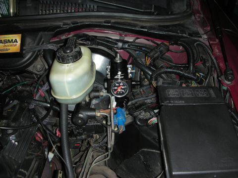 1992 Ford Crown Victoria - Close-up of a fuel pressure regulator and brake fluid reservoir in a vehicle's engine bay.