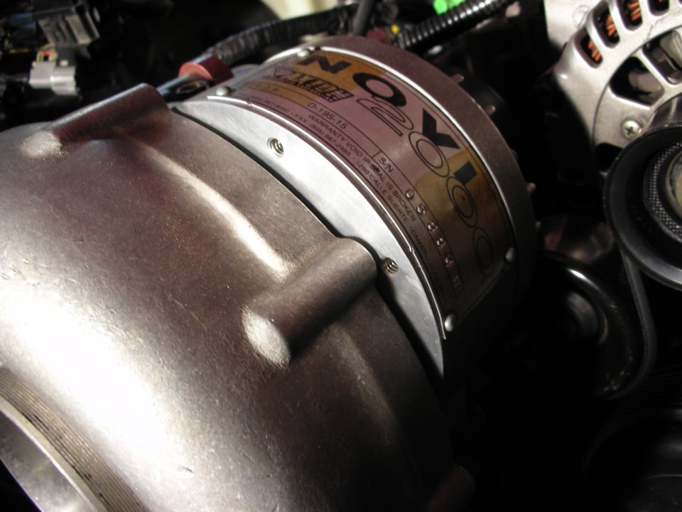 Close-up of a Novi supercharger with a metal tag showing serial number and warranty information