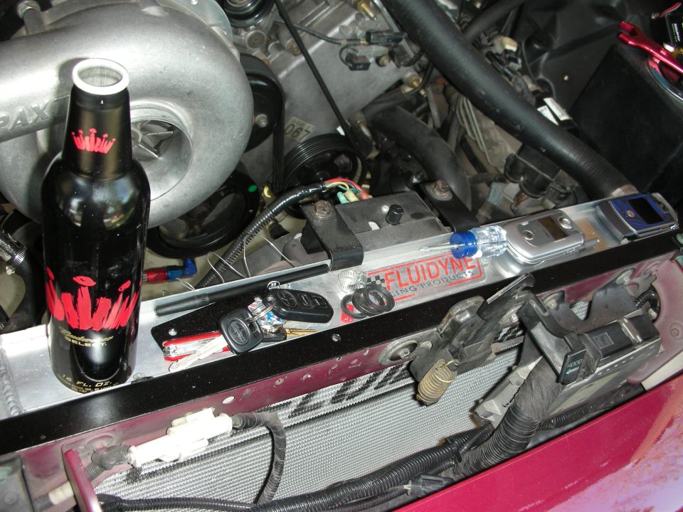 Engine bay with a black beer bottle, car keys, and a Fluidyne radiator