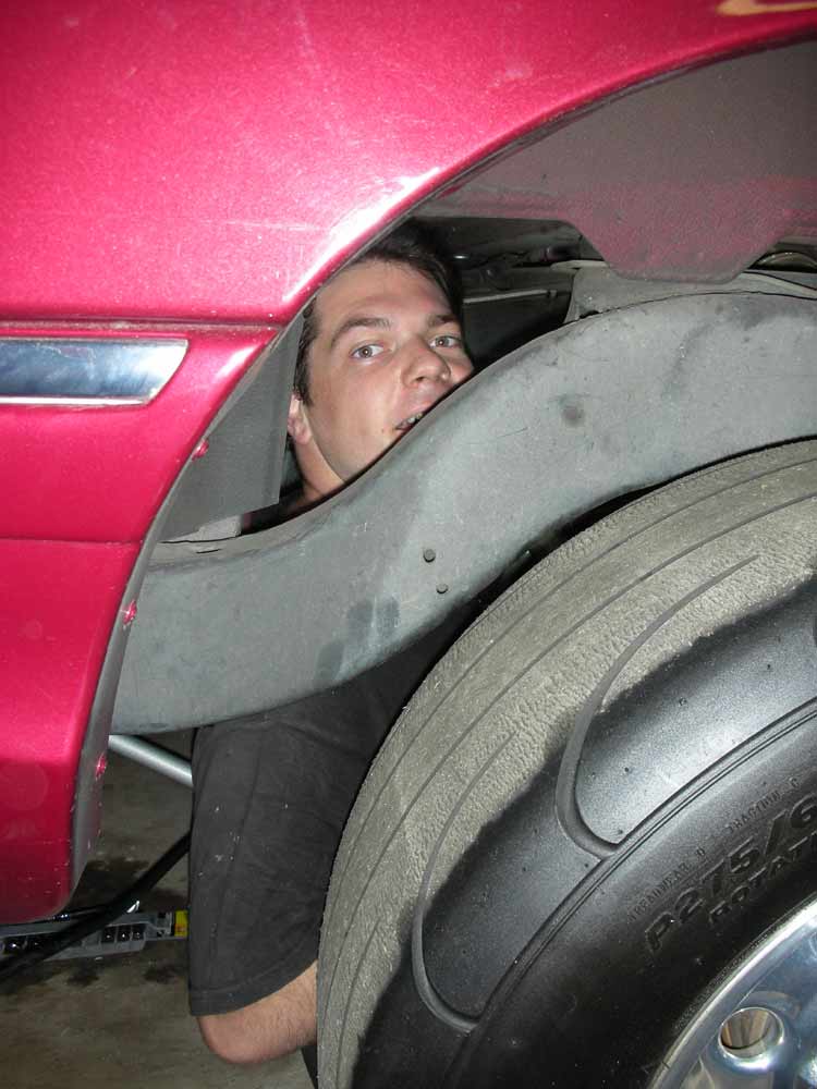 Man peers out from under the wheel well of a red car