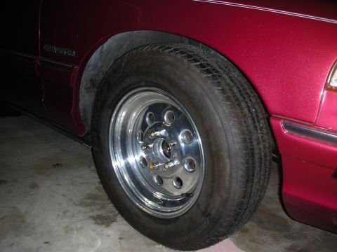 1992 Ford Crown Victoria - The wheel and fender of a red sedan are shown, with a 'GRAND MARQUIS' badge visible on the body.