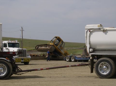 1986 Ford Bronco - An excavator is being loaded onto a trailer, with other trucks present at the scene.