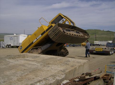1986 Ford Bronco - A large yellow excavator is stuck at an odd angle on a concrete structure, with a person observing the situation.
