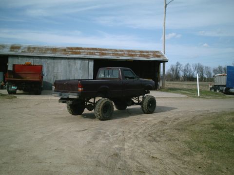 2001 Dodge 2500 - A lifted maroon pickup truck sits on a dirt lot in front of a barn, with another truck visible in the background.