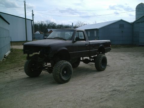 2001 Dodge 2500 - A dark, heavily modified pickup truck with oversized tires sits in a dirt lot, its front grille removed.