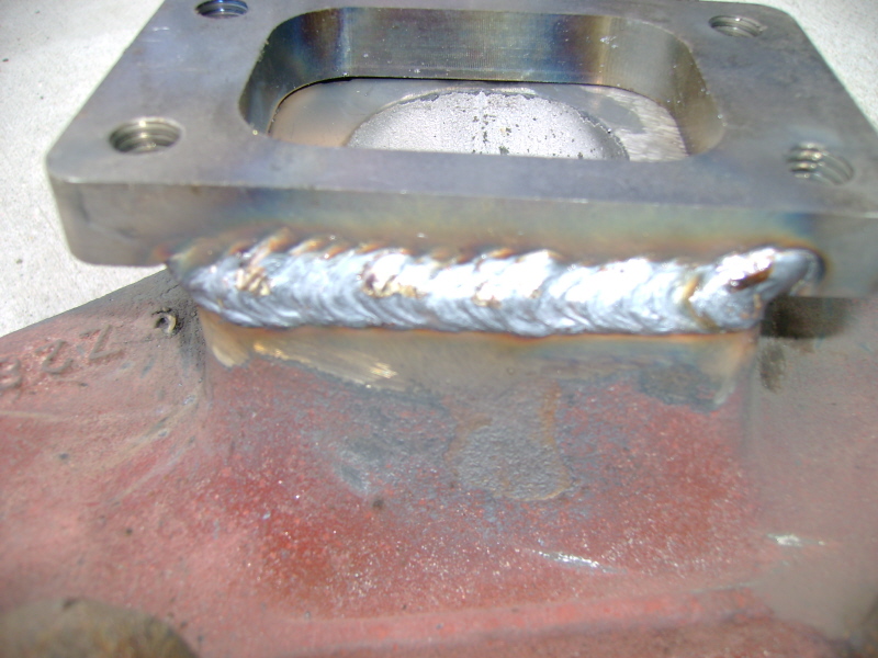 MIG weld bead joining a machined adapter plate to a red-primered cast intake manifold