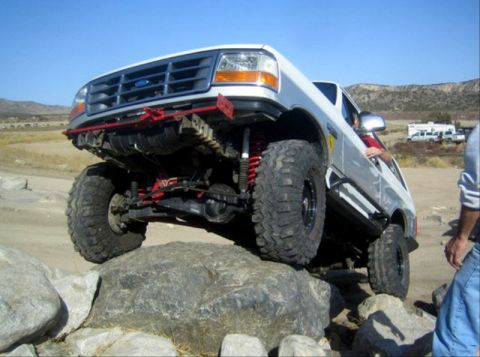 1996 Ford Bronco - A white Ford Bronco navigates a rocky off-road course with its front tire high in the air.
