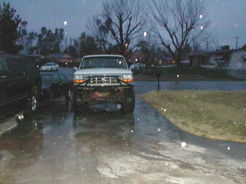1996 Ford Bronco - A white Ford truck with a custom bumper is parked on a wet driveway during a rain shower.