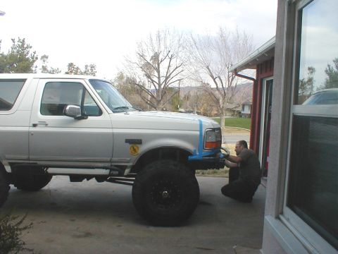 1996 Ford Bronco - A man works on the front bumper of a silver Ford Bronco with oversized tires.