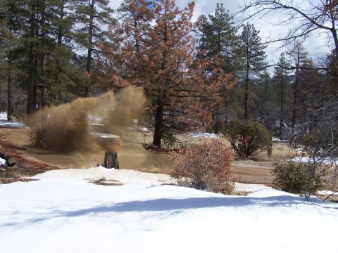 1996 Ford Bronco - A white SUV drives through a dusty, muddy area with snow on the ground, surrounded by trees.