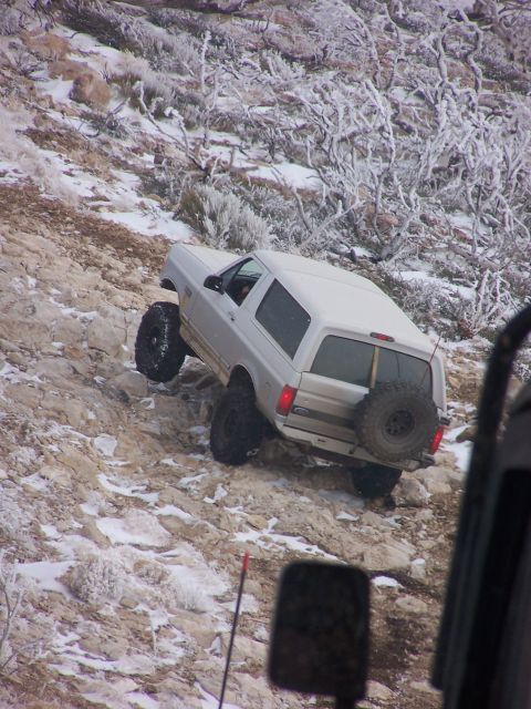 1996 Ford Bronco - A 1996 Ford Bronco navigates a challenging, snow-dusted rocky incline, with another vehicle's mirror in view.