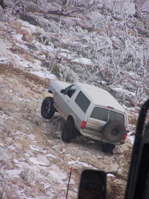 1996 Ford Bronco - A white Ford Bronco navigates a challenging rocky incline covered in snow and frost.