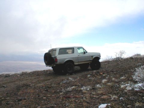 1996 Ford Bronco - A silver 1996 Ford Bronco is parked on a dirt hill under a cloudy sky, with a spare tire mounted on the rear.