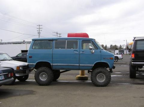 1983 Ford Ranger - A lifted blue van is parked in a lot with other vehicles under an overcast sky.