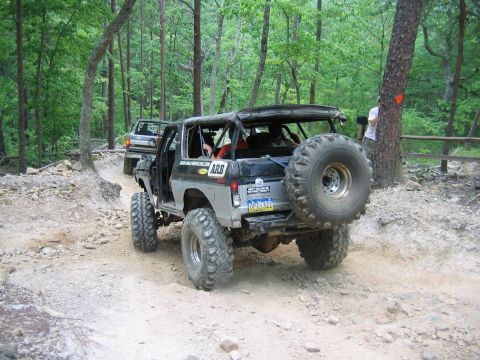 1992 Ford Mustang - Two off-road vehicles navigate a wooded trail with steep inclines and loose dirt.