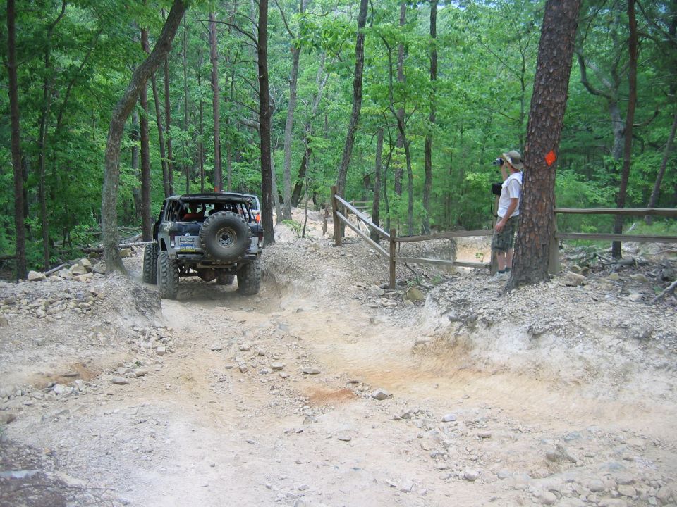 Off-road vehicle with spare tire on rear, navigating a wooded dirt trail